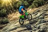 Three-quarter rear angle of a person riding a motorcycle uphill off-road.
