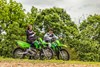 Side angle of two people seated on separate stationary motorcycles off-road.