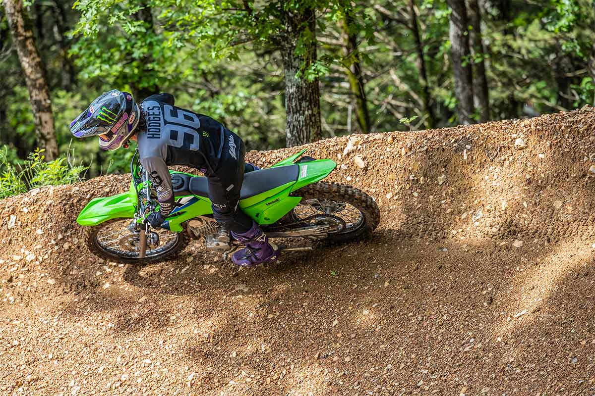 Side angle of a person riding a motorcycle around a bend on an off-road course.