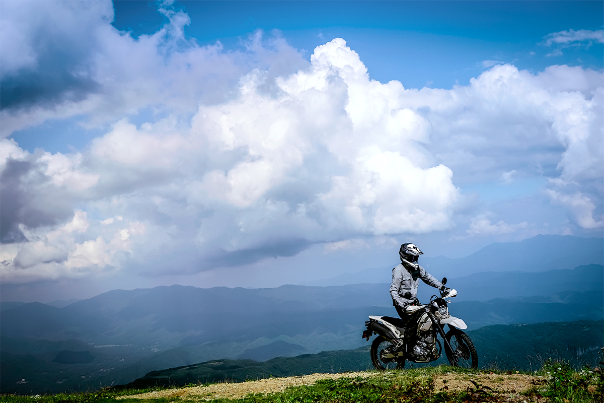 Three-quarter front angle of a person riding a silver motorcycle off-road.