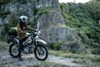 Side angle of a person seated on a stationary motorcycle off-road.