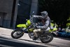 Side angle of a person riding a green motorcycle on a city street.