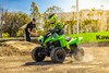 Three-quarter front angle of a person riding a green ATV on a closed course under adult supervision.