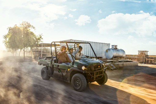 Three-quarter front angle of three people riding in a side x side at a jobsite. opens in a new window