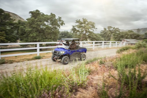 Three-quarter front angle of a person and passenger driving a side x side on a dirt trail. opens in a new window