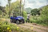 Three-quarter front angle of two people working next to a side x side parked on a trail.