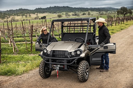 Three-quarter front angle of a two people entering a side x side off-road. opens in a new window