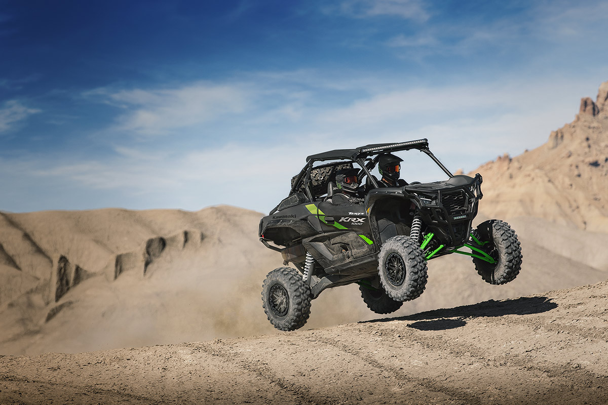 Three-quarter front angle of two people driving a side x side off-road.