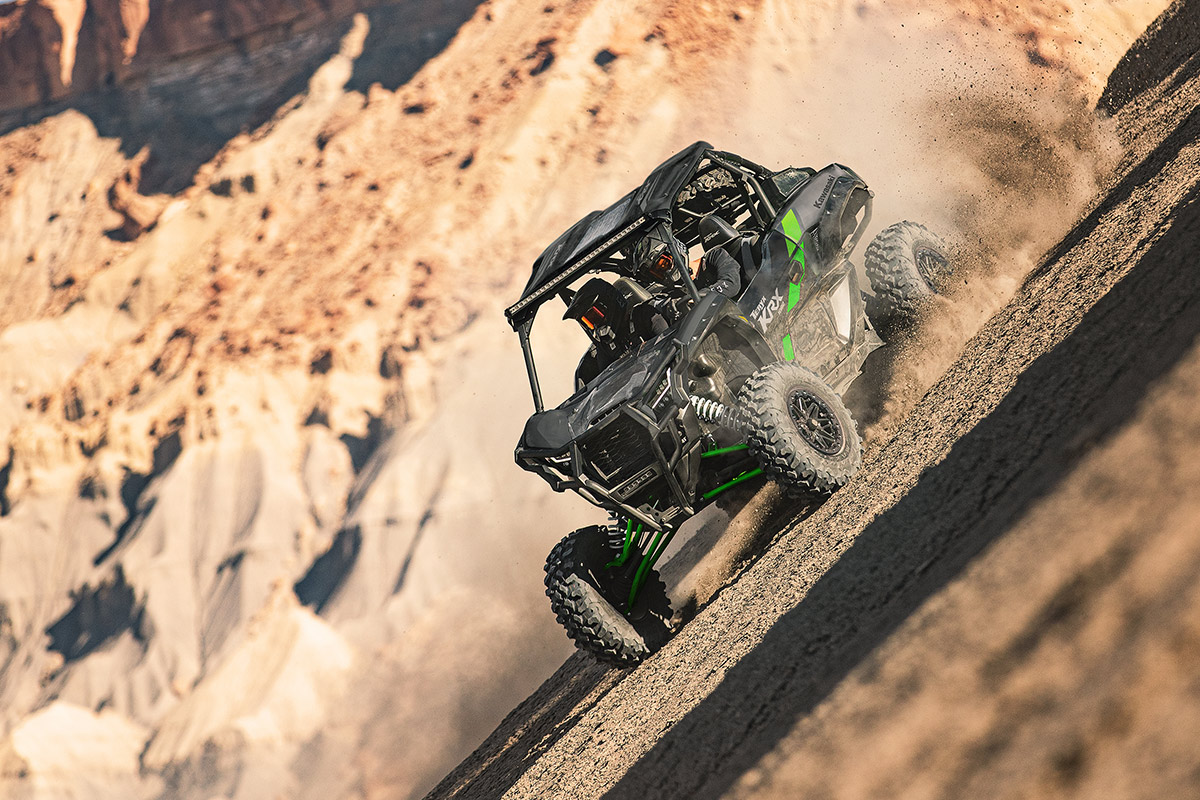 Three-quarter front angle of two people driving a black side x side off-road.