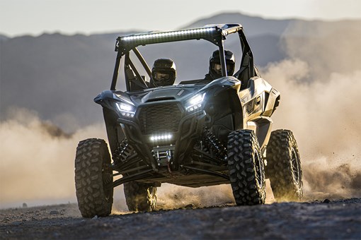 Front angle of two people driving a side x side off-road. opens in a new window