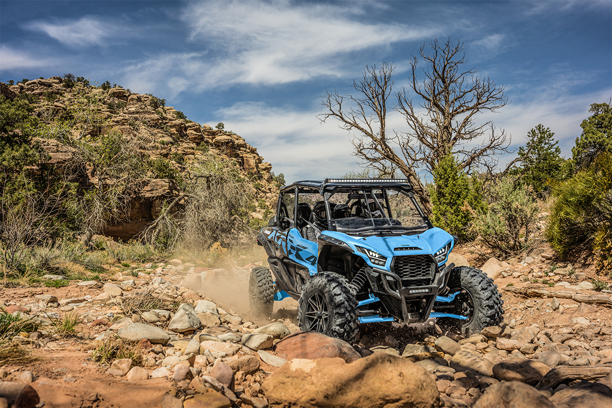 Three-quarter front angle of four people driving a side x side off-road.