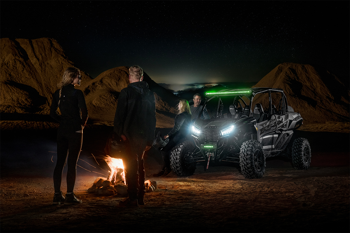 Three-quarter front angle of a side x side parked off-road near four people.