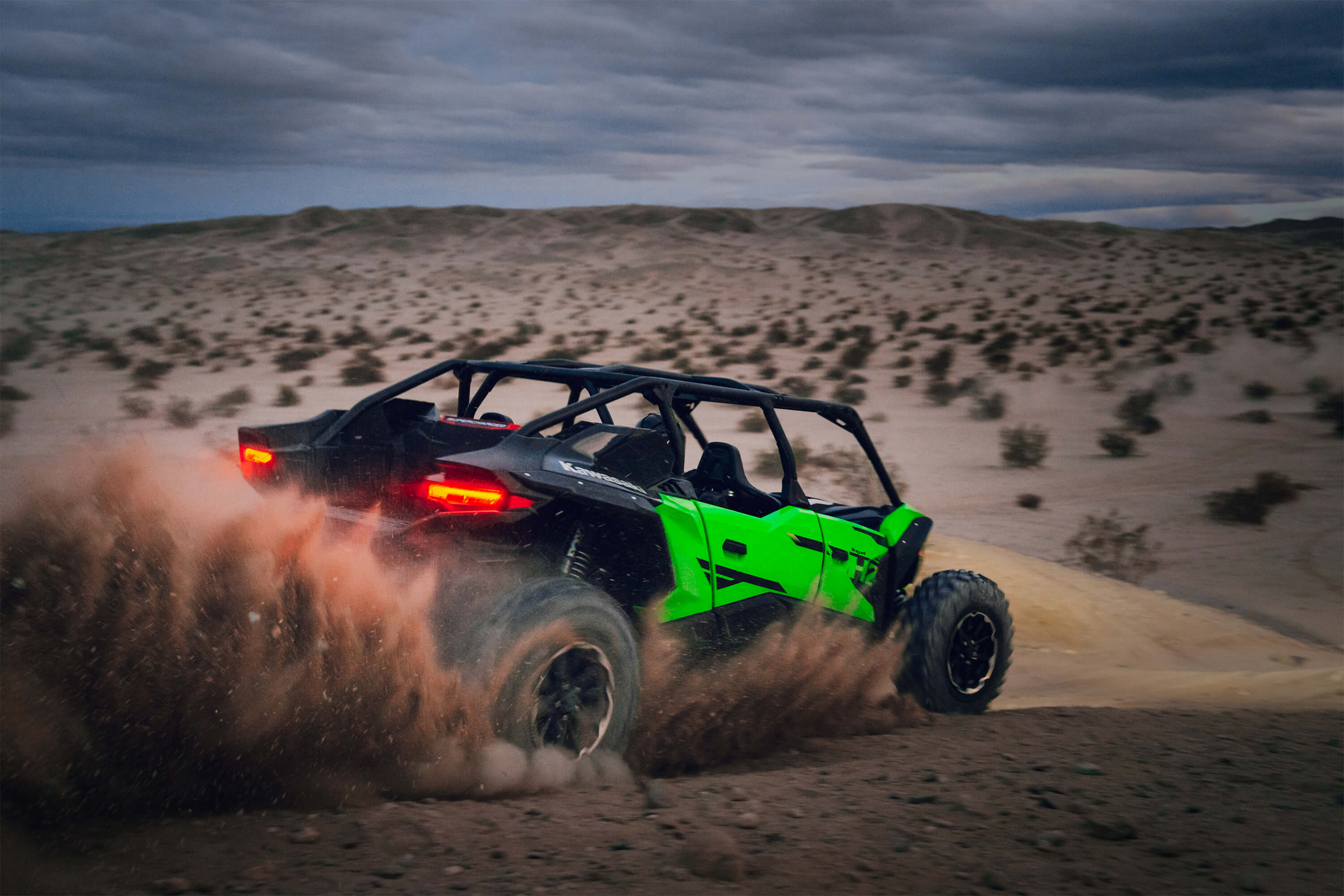 Rear angle of a person driving a side x side off-road kicking up sand.