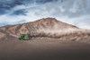 Side angle of a person driving a side x side off-road at the bottom of a large dune.