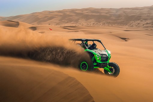 Profile angle of a person driving a side x side off-road kicking up sand. opens in a new window