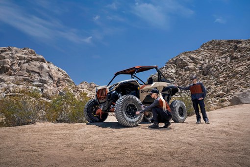 Three-quarter front angle of two people checking front-left tire pressure on a side x side. opens in a new window