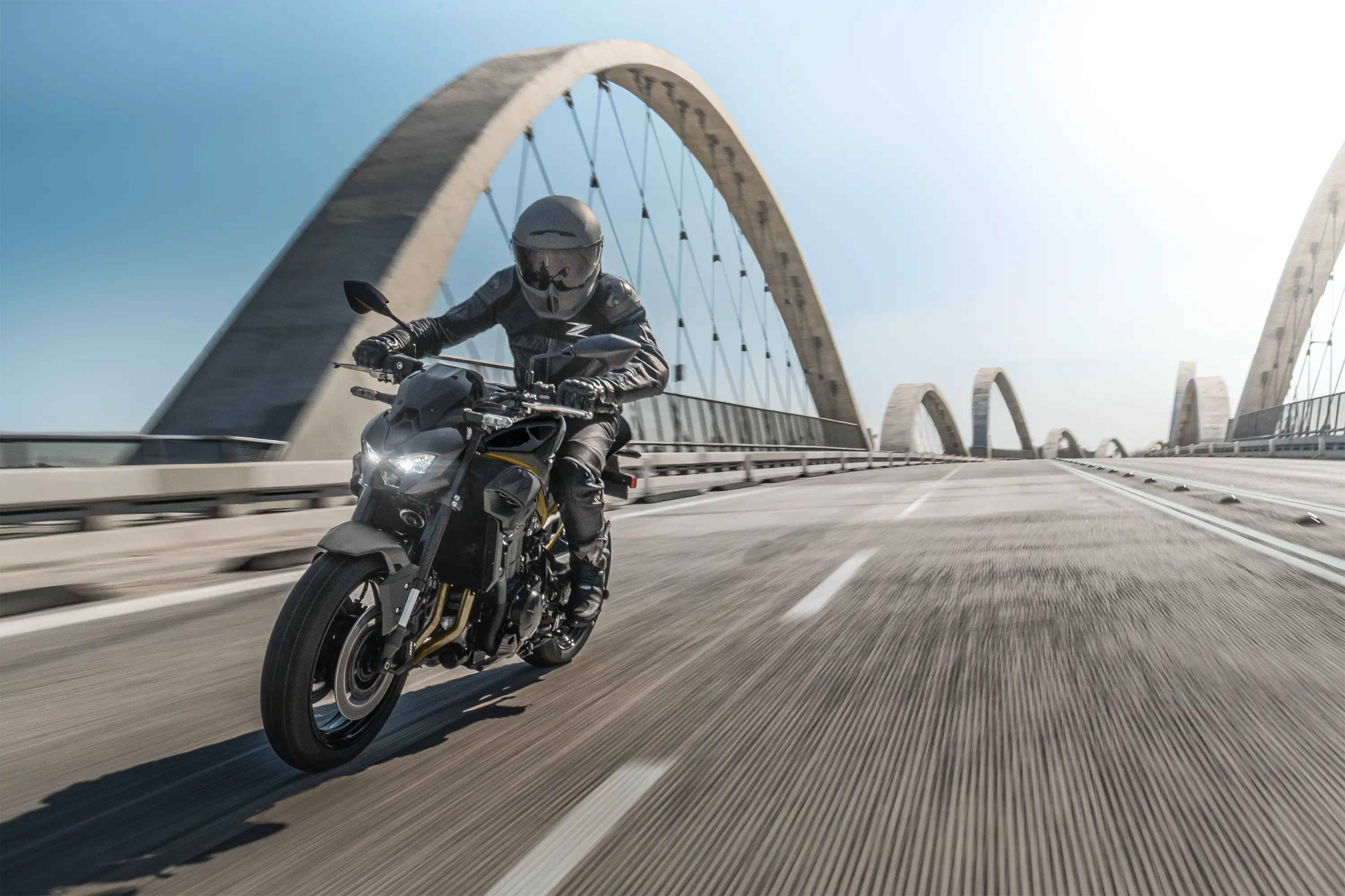 Three-quarter front angle of a person riding a motorcycle on a bridge.