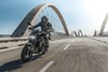 Three-quarter front angle of a person riding a motorcycle on a bridge.