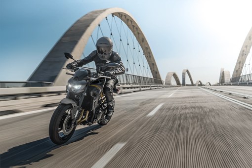 Three-quarter front angle of a person riding a motorcycle on a bridge. opens in a new window