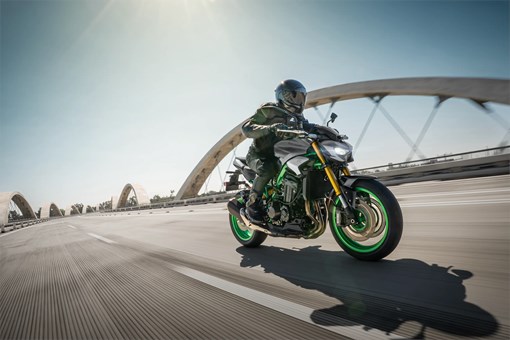 Three-quarter front angle of a person riding a motorcycle on a bridge. opens in a new window