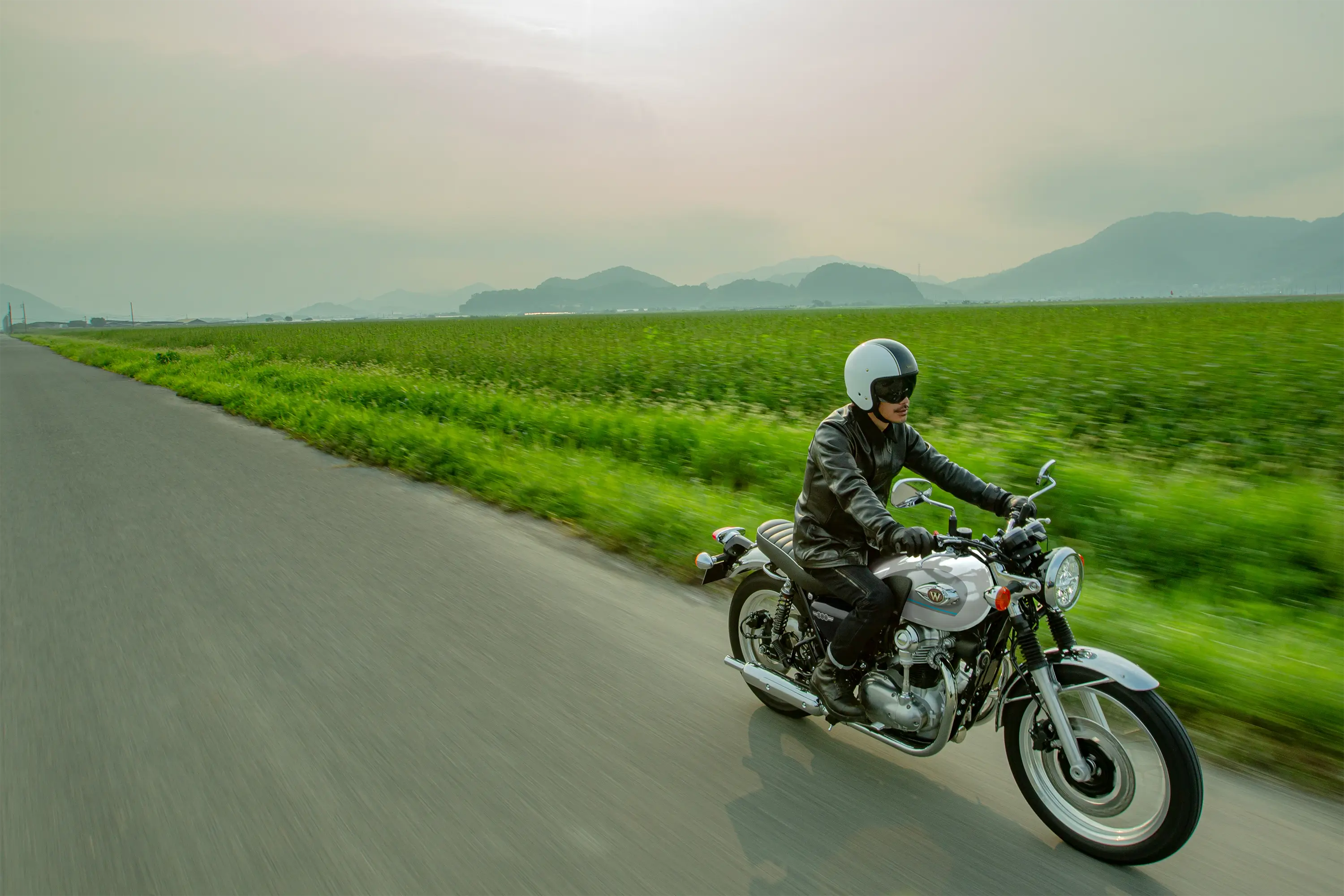 Three-quarter front angle of a person riding a motorcycle next to a field.