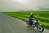Three-quarter front angle of a person riding a motorcycle next to a field.