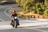 Front three-quarter angle of a person riding a motorcycle over a bridge.
