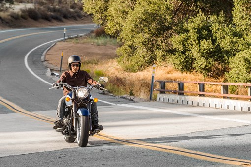 Front three-quarter angle of a person riding a motorcycle over a bridge. opens in a new window