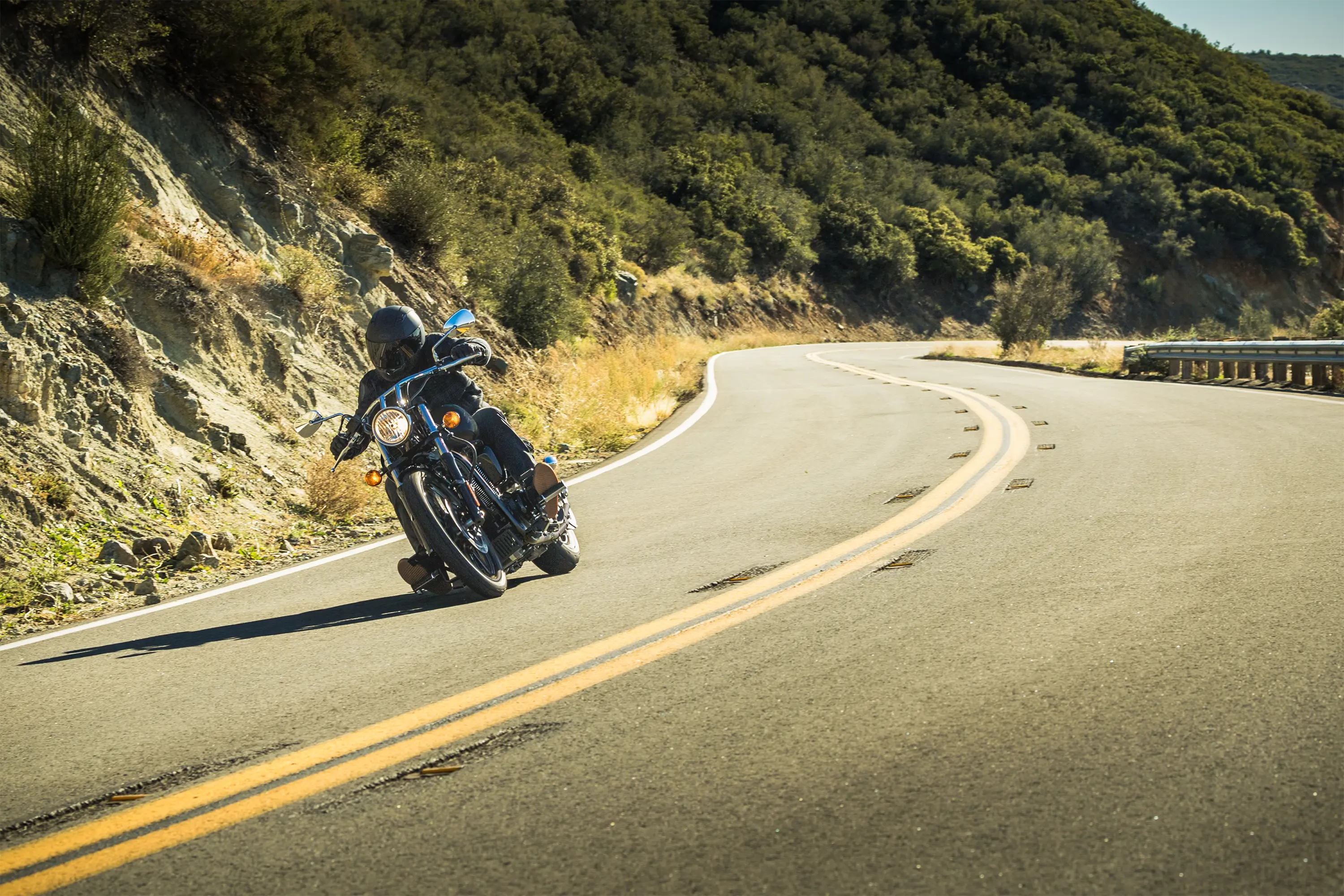 Front three-quarter angle of a person riding a motorcycle on a curvy highway.
