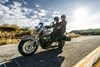 Three-quarter front angle of two people riding a motorcycle on a highway.
