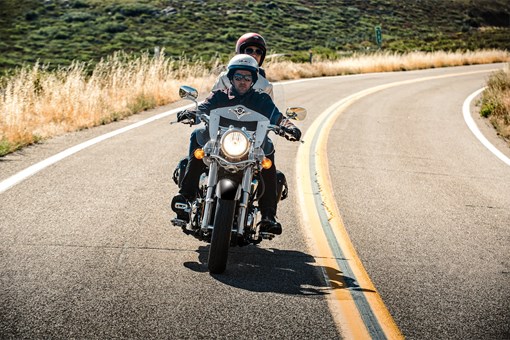 Front angle of two people riding a motorcycle on a highway. opens in a new window