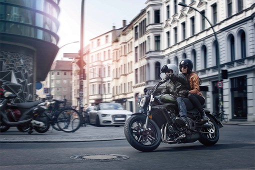 Three-quarter front angle of two people riding a motorcycle on the street. opens in a new window