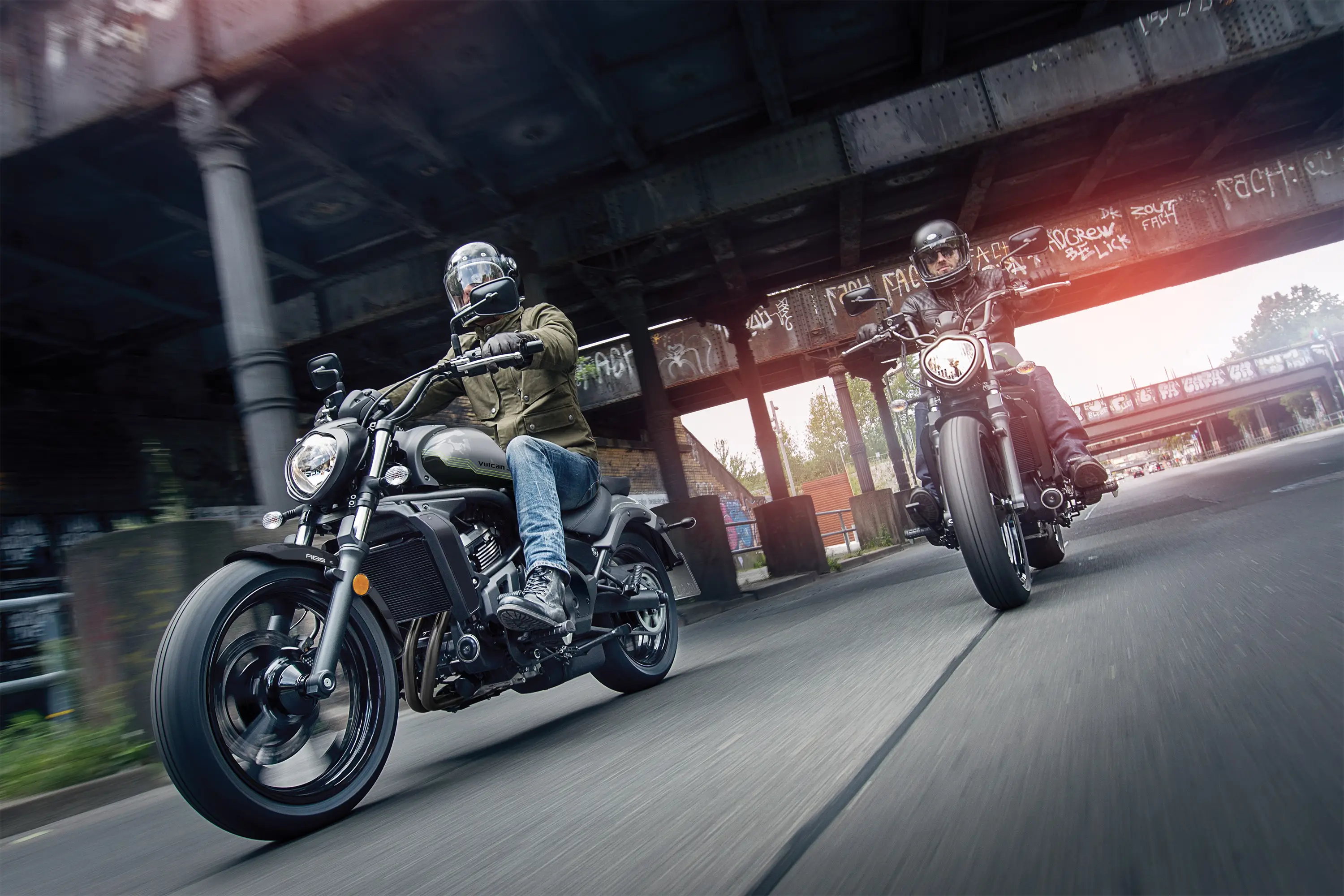 Three-quarter front angle of two people riding motorcycles on the street.