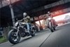 Three-quarter front angle of two people riding motorcycles on the street.