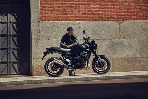 Profile angle of a motorcycle parked on a city sidewalk near a person. opens in a new window