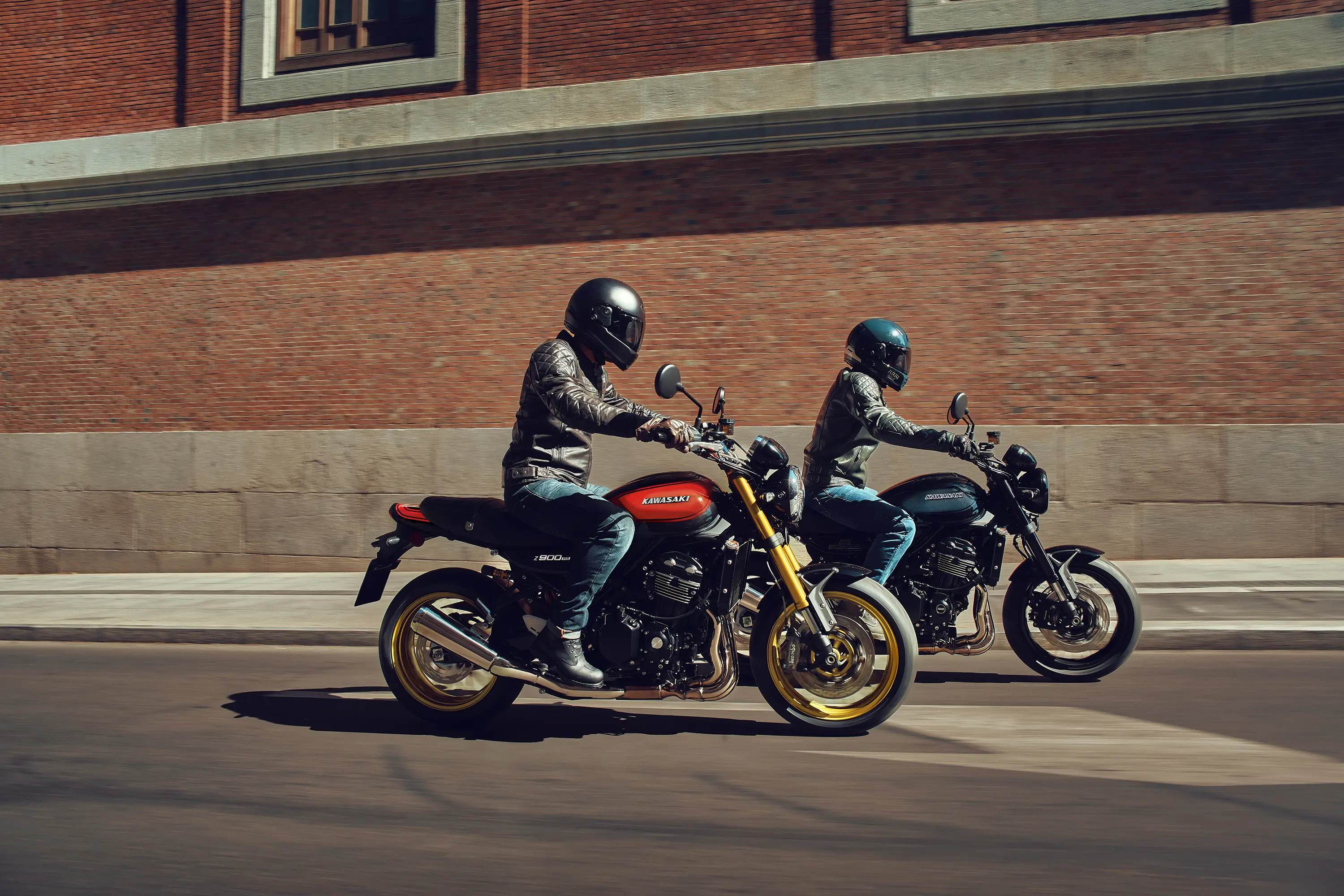 Side angle of two people riding separate motorcycles on a city street.