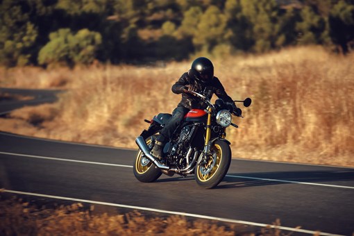 Profile view of a person riding a motorcycle on a road. opens in a new window