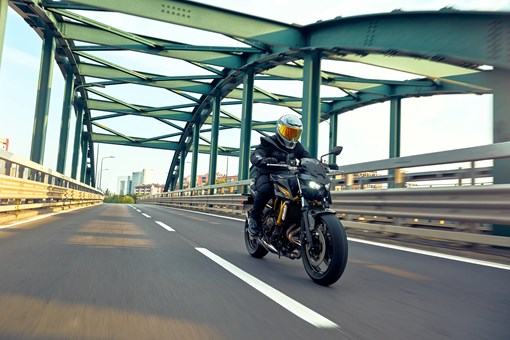 Three-quarter front angle of a person riding a motorcycle on a bridge. opens in a new window