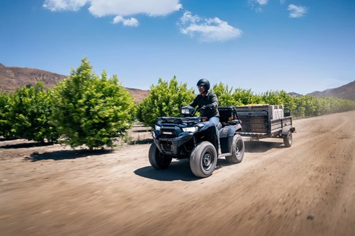 Three-quarter front angle of a person driving an ATV with a trailer in tow. opens in a new window