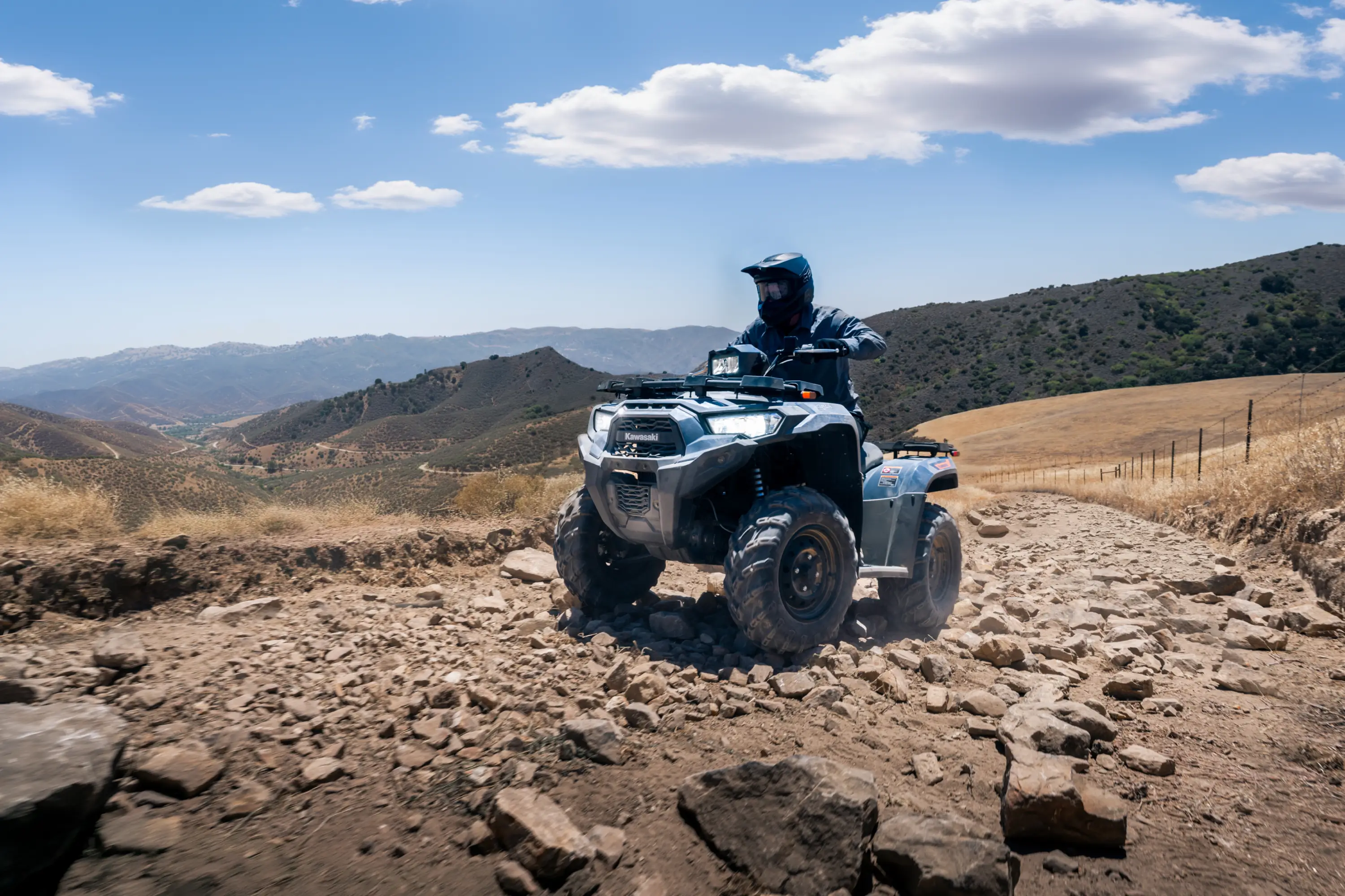 Three-quarter front angle of a person driving an ATV up a ridge.