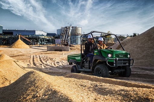 Three-quarter front angle of two people riding in a side x side on a jobsite. opens in a new window