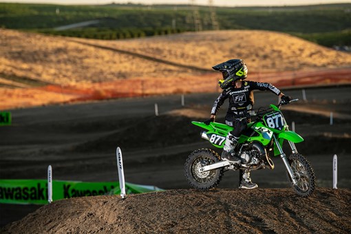Kid parked on a green dirt bike on a motocross bike looking over his shoulder. opens in a new window