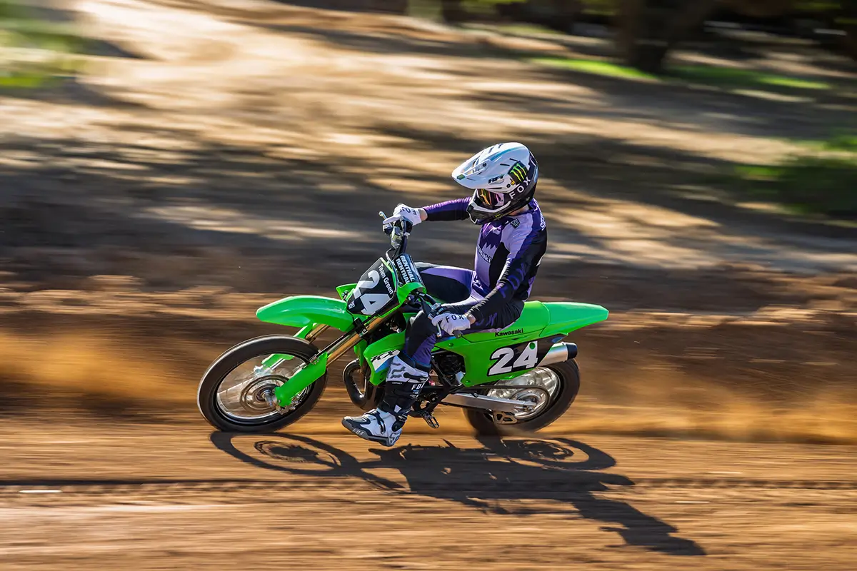 Left side view of a person riding a green dirt bike fast on a motocross track.
