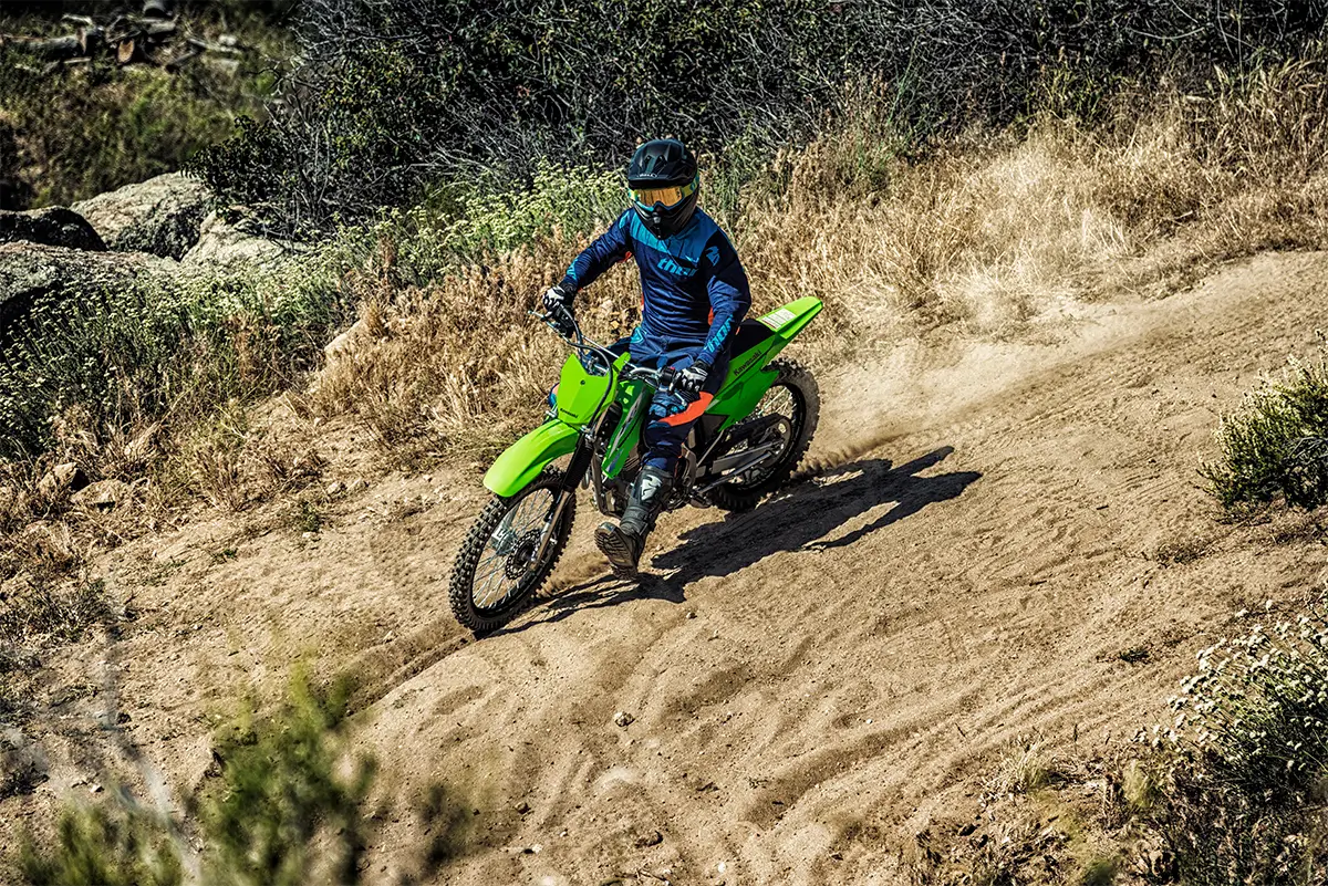 Front three-quarter right view of a person riding a green dirt bike off-road.