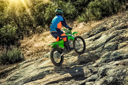 Rear three-quarter view of a person riding a green dirt bike up a rock face. opens in a new window