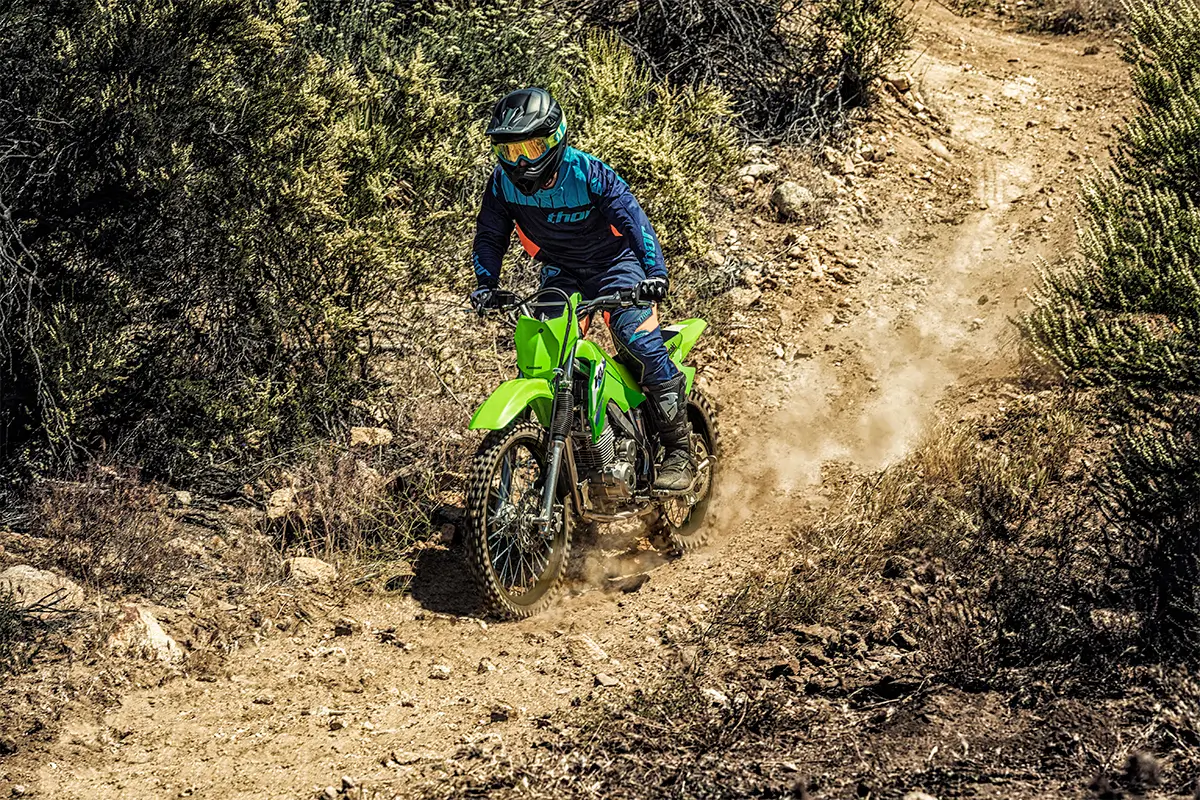 Oncoming view of a person riding a green dirt bike down a rocky trail.
