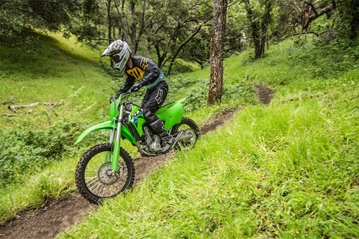 A person riding a green off-road dirt bike down a trail in a green forest. opens in a new window