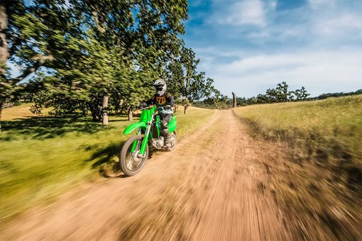 Oncoming view of a person riding a green off-road dirt bike down a dirt road. opens in a new window