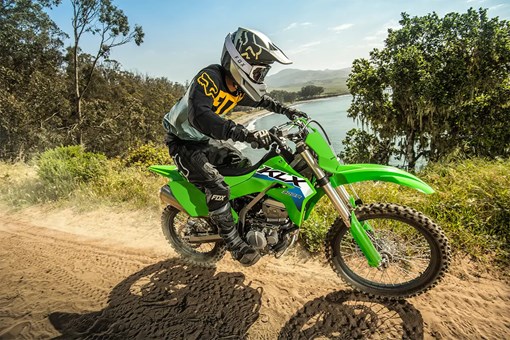 Right side view of a person riding a green dirt bike down a scenic trail overlooking the ocean. opens in a new window