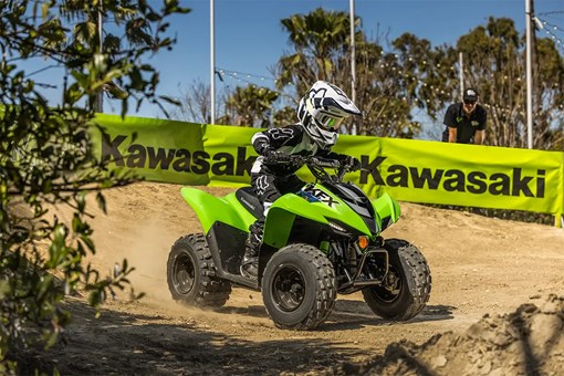 A kid riding a green youth ATV on a motocross track. opens in a new window